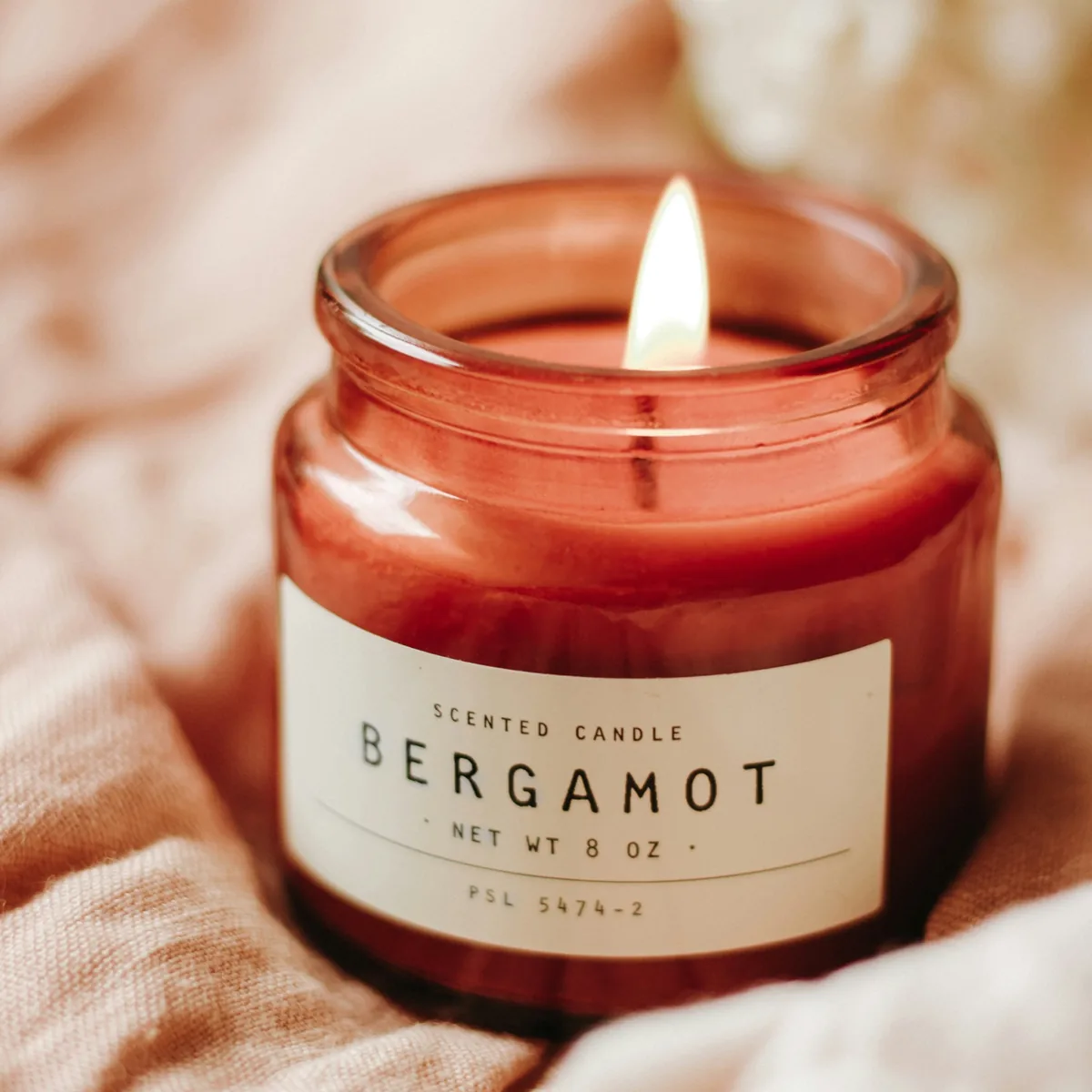 Original photo: a red glass candle jar labelled Bergamot, resting on pink linen